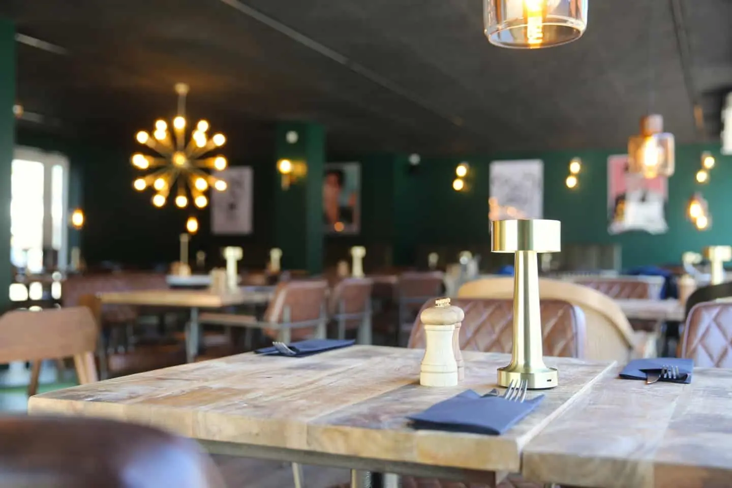The dining room at Café B with green walls, brass lamps and wooden tables